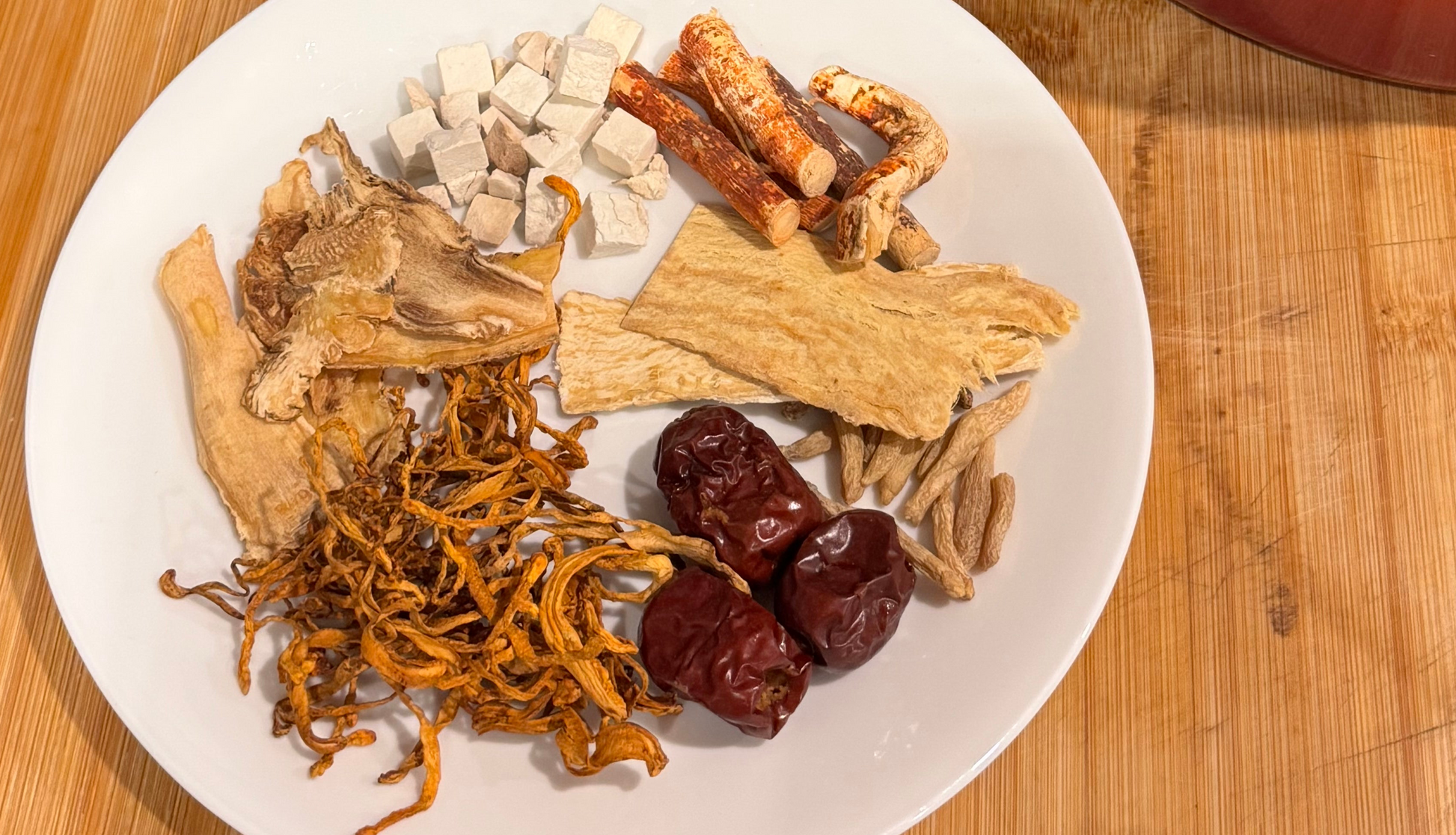 Red pot on a wooden surface with a plate of dried mushrooms and other ingredients.