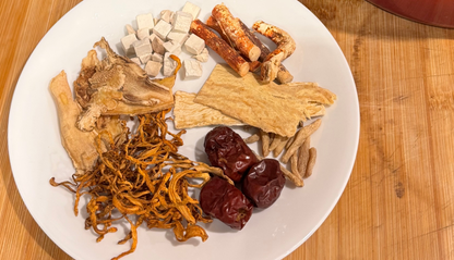 Red pot on a wooden surface with a plate of dried mushrooms and other ingredients.