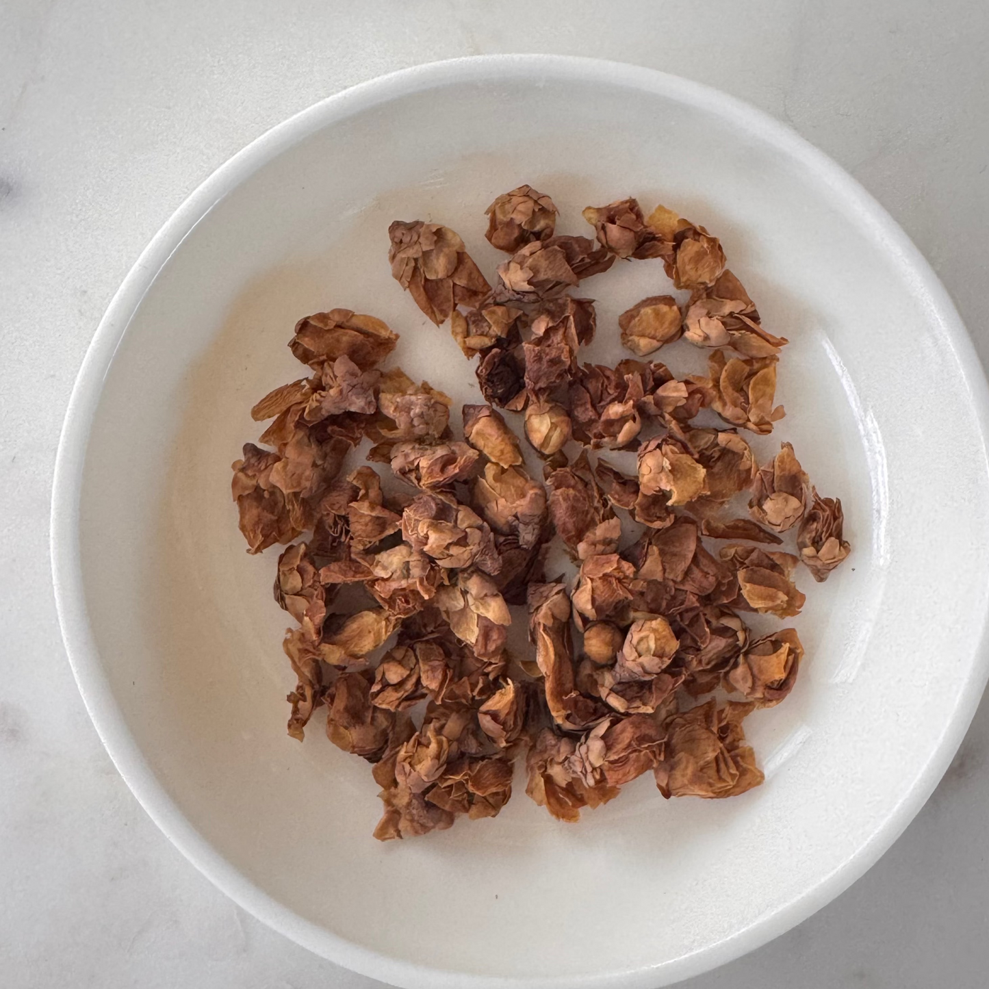 Dried peach flowers in a white bowl on a light background